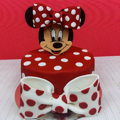 Seitenansicht der fertig dekorierten Minnie Maus Geburtstagstorte, bedeckt mit rotem Fondant und aufwendigen Verzierungen.