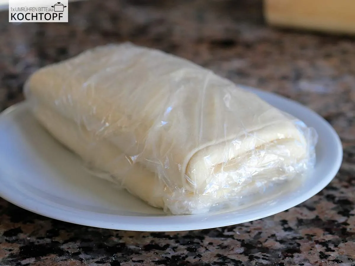 Selbstgemachter Blätterteig sorgfältig in Klarsichtfolie verpackt, ruhend im Kühlschrank, um Austrocknen zu verhindern.