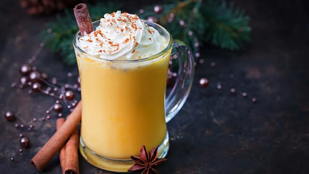 Selbstgemachter Eierpunsch mit Sahnetopping und Zimtpulver in einem Glas, perfekt für die Weihnachtszeit