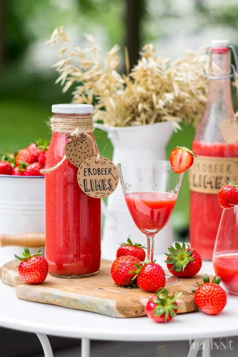 Selbstgemachter Erdbeerlimes in Flaschen, präsentiert auf einem Gartentisch im Grünen, ideal für den Sommer