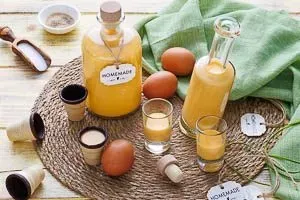 Servierfertiger Eierlikör in Gläsern mit Waffeln und frischen Blumen