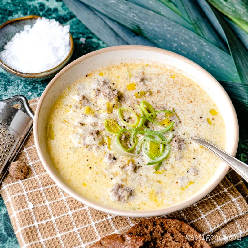 Servierte Käse-Lauch-Suppe mit Hackfleisch und frischem Baguette auf einem Holztisch