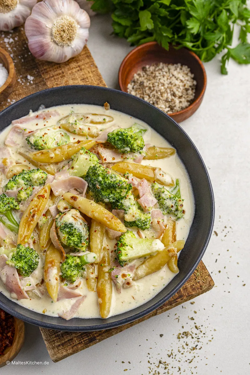 Serviertes Schupfnudel-Gericht mit Kochschinken, Brokkoli und Käsesauce, garniert mit frischer Petersilie