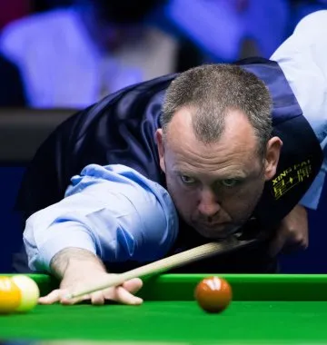 Snookerspieler zielt mit seinem Queue auf eine Kugel auf dem grünen Tisch, exemplarisch für eine englische Sportart mit Schläger