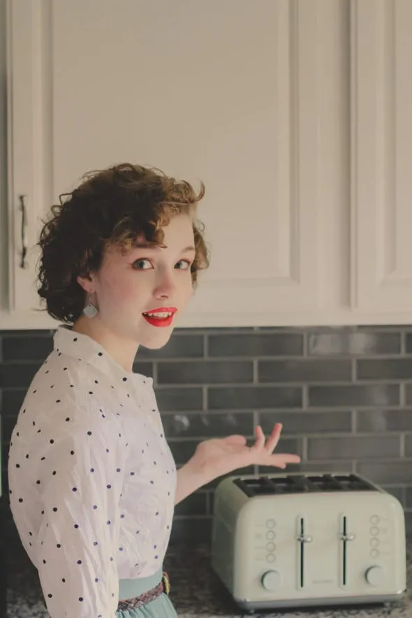 Sonia steht vor einem Buydeem Toaster und lächelt in die Kamera