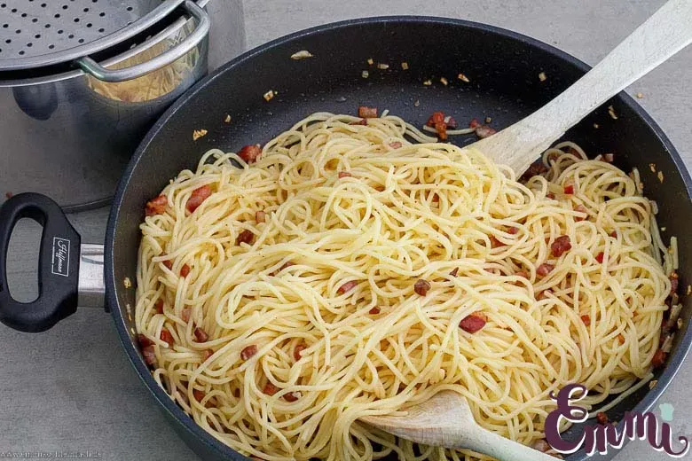 Spaghetti werden in der Pfanne mit dem ausgelassenen Speckfett vermengt, um die perfekte Grundlage für die Carbonara zu schaffen.