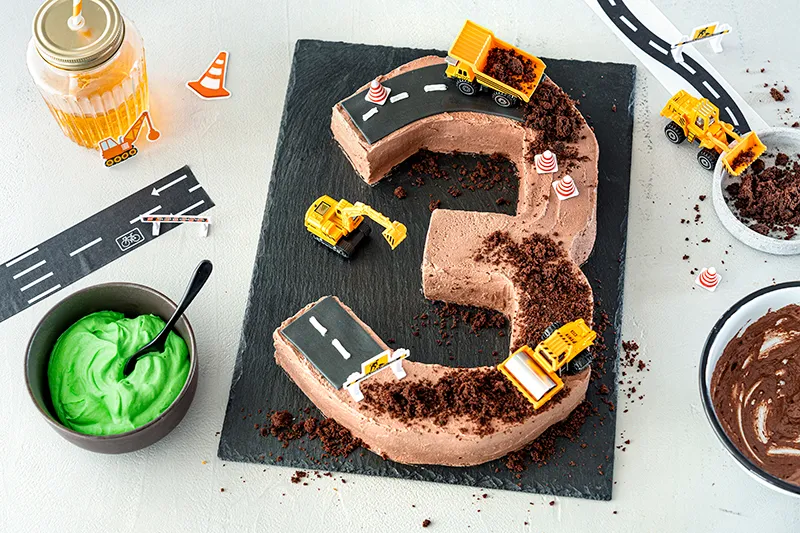 Spielzeugbagger und Kuchenbrösel als Erdhaufen auf dem Baustellenkuchen arrangieren