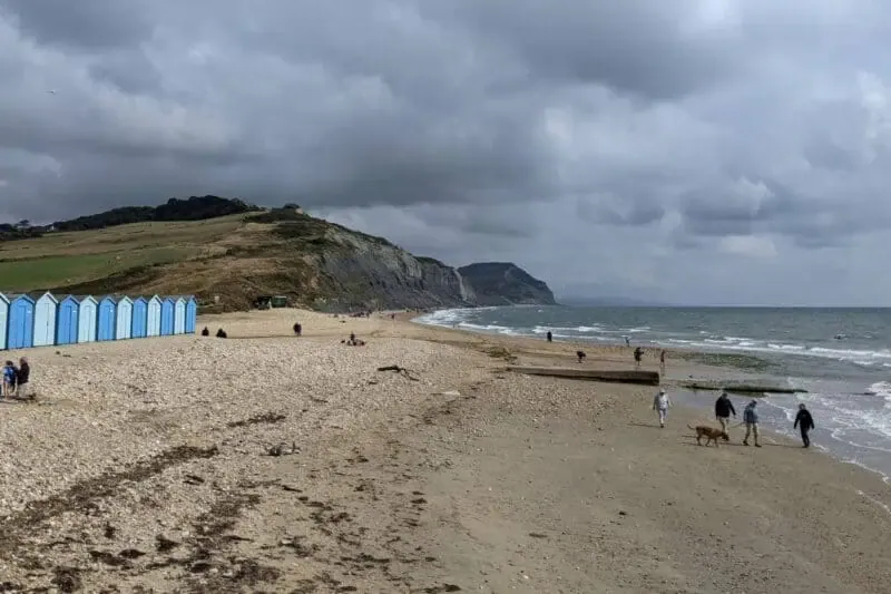 Strand mit schwarzen Klippen und blauen Badehäusern in Charmouth an der Jurassic Coast