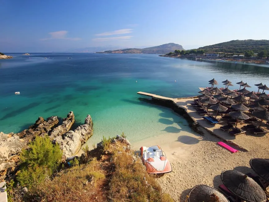 Strand von Ksamil in Albanien mit türkisfarbenem Meer, Sonnenschirmen und leeren Liegen, bereit für entspannte Urlaubstage.
