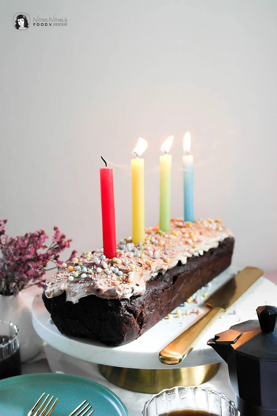 Stück Schoko-Brownie Kastenform Kuchen auf einem Teller, mit bunten Streuseln und einer Kerze für Feierlichkeiten.