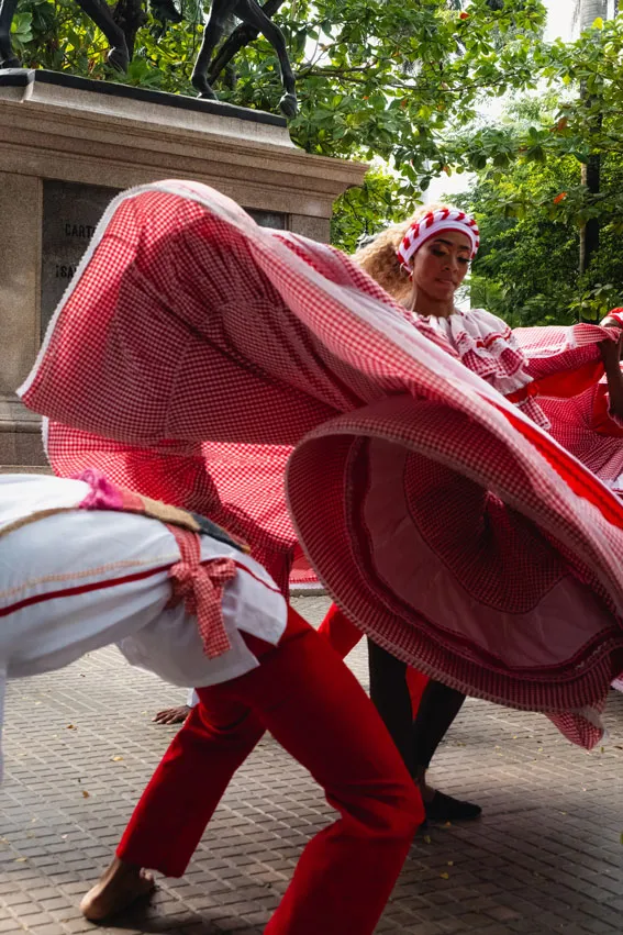 Tänzer und Tänzerinnen in traditionellen rot-weißen Trachten in schwungvollen Bewegungen unter freiem Himmel bei einem Fest