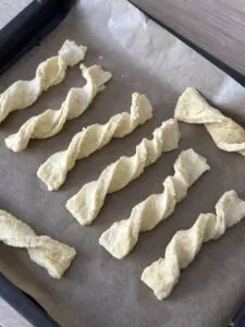 Teigstreifen für Käsestangen werden verdreht und auf ein Backblech gelegt, bevor sie gebacken werden.