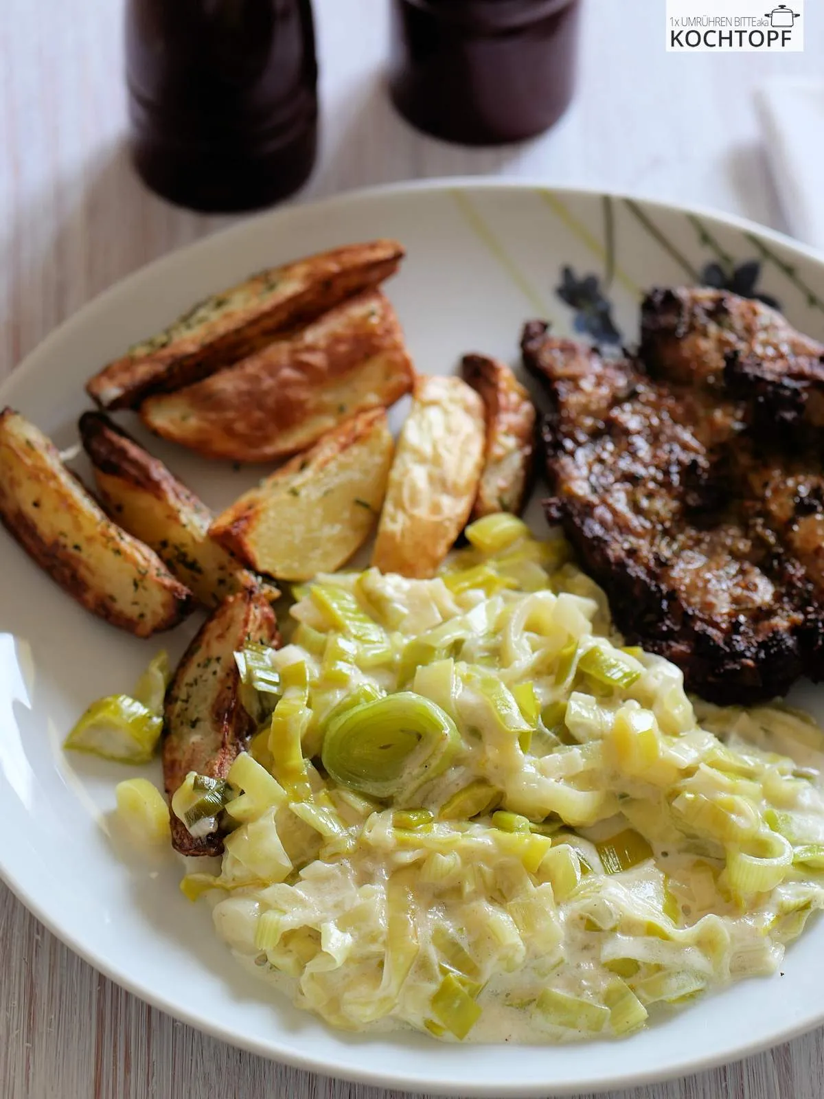 Teller gefüllt mit Rahmlauchgemüse, knusprigen Kartoffel-Wedges und einem gebratenen Nackensteak, bereit zum Genießen.