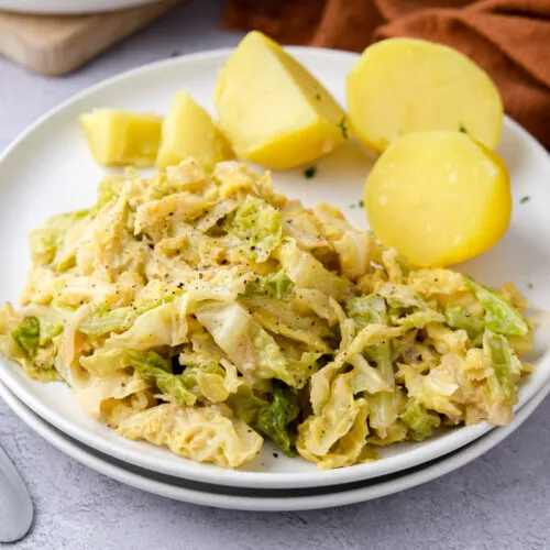 Teller mit cremigem Wirsing neben Salzkartoffeln mit orangefarbenem Tuch im Hintergrund