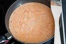 Tomaten-Sahnesoße köchelt in einem Topf auf dem Herd, mit Zwiebeln und Knoblauch.