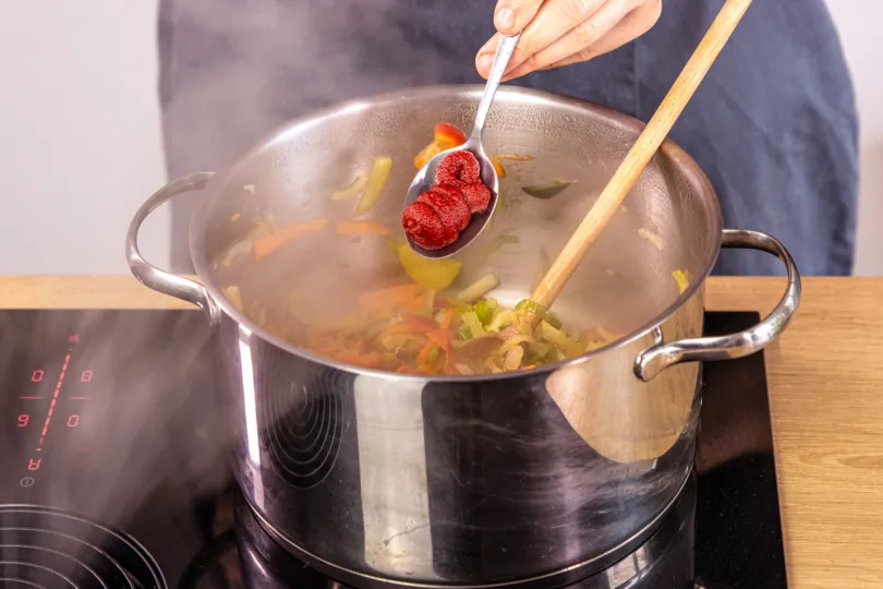 Tomatenmark wird in die vegetarische Soljanka eingerührt, um die Basis zu würzen