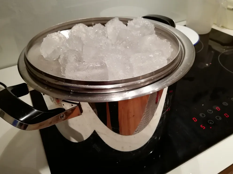 Topf mit umgedrehtem Deckel, bedeckt mit Eis, für die hausgemachte alkoholfreie Gin-Destillation