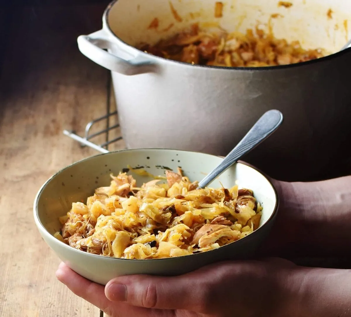 Traditionelles Bigos Gericht in einer grünen Schale mit Löffel, im Hintergrund ein Topf mit Krauteintopf.