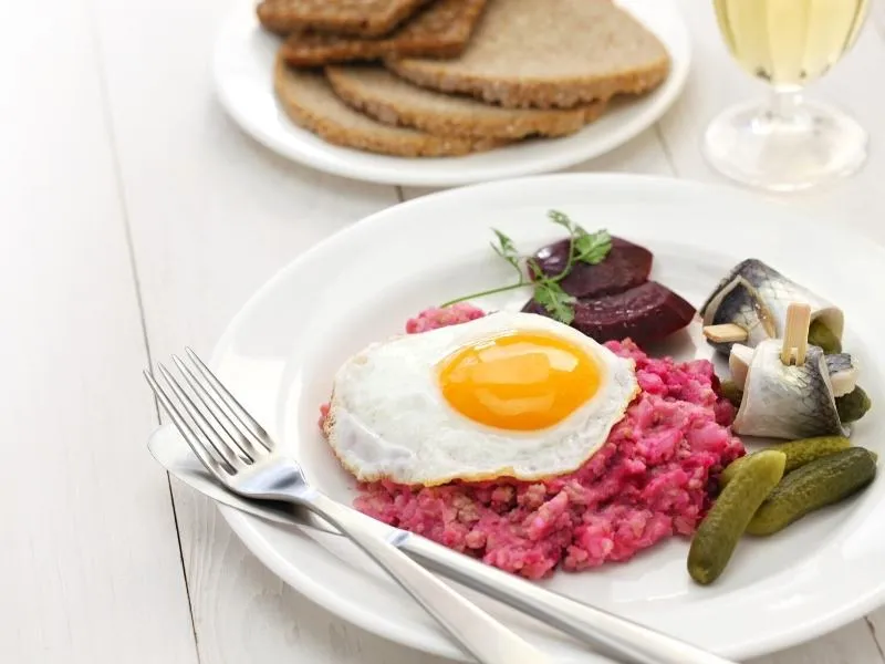 Traditionelles Labskaus mit Roter Bete, Spiegelei und Matjesfilet auf einem Teller.