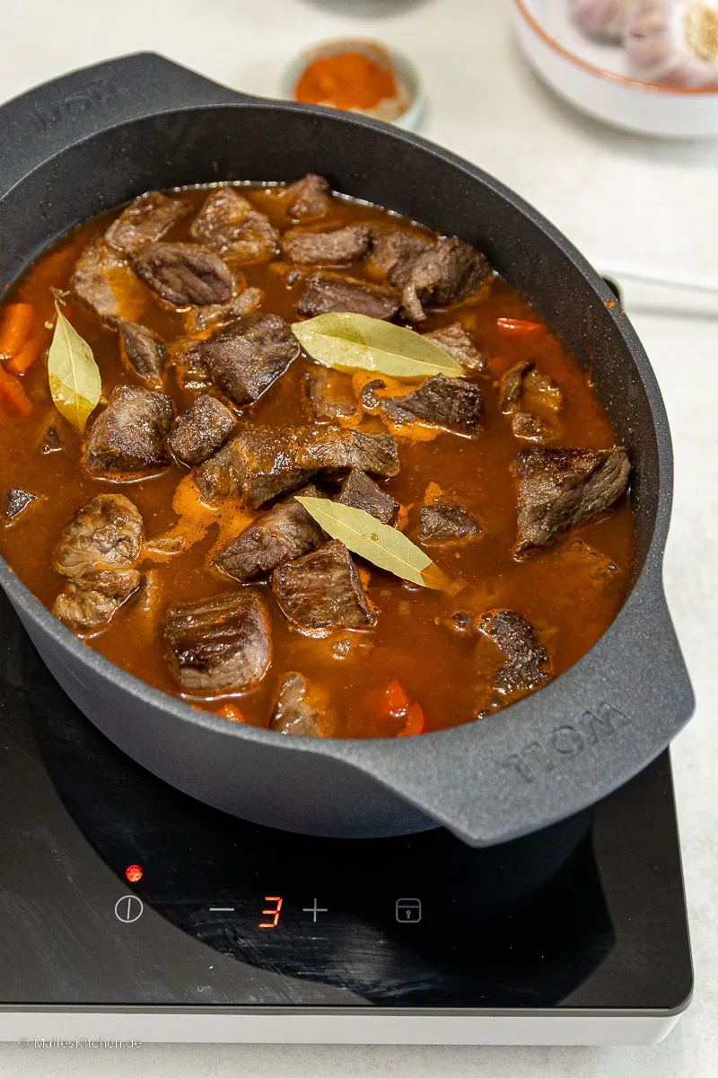 Ungarisches Gulasch köchelt langsam in einem Topf, die Sauce verdickt sich zu einer sämigen Konsistenz.