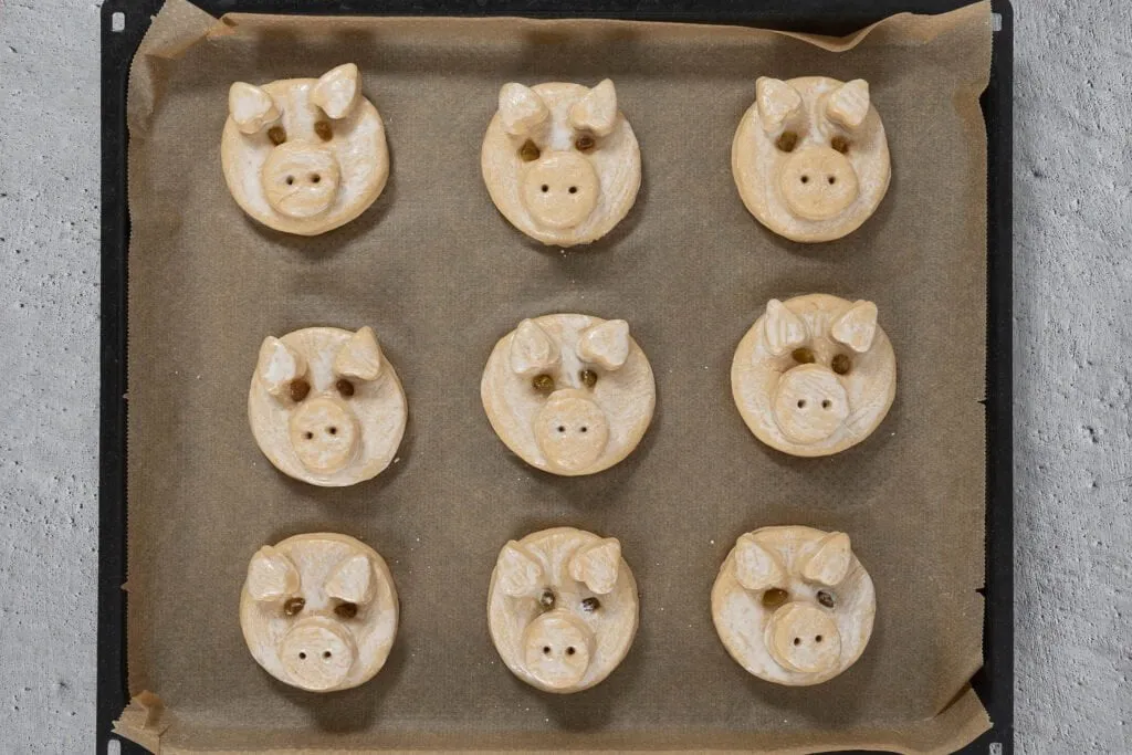 Ungebackene Glücksschweinchen aus süßem Hefeteig, sorgfältig geformt auf dem Backblech.