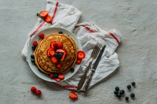 Vegane Leinsamen-Pancakes gestapelt auf einem Teller mit Ahornsirup und Beeren.