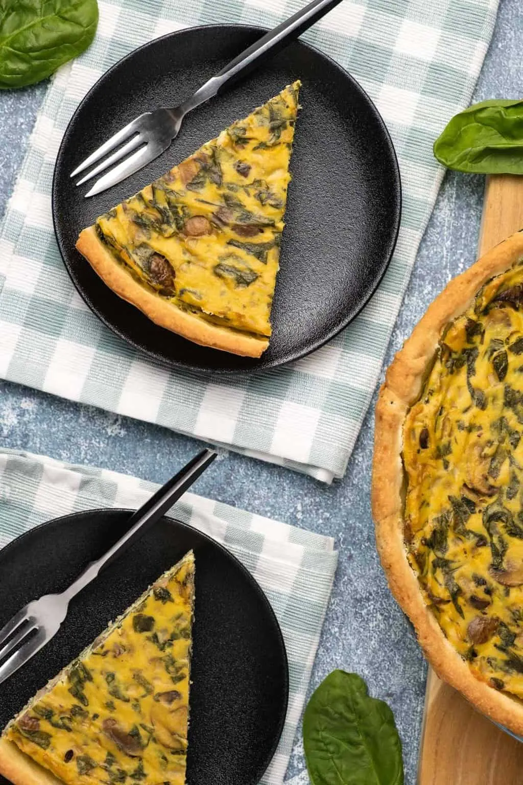 Vegane Quiche in Scheiben auf schwarzen Tellern mit Gabeln.
