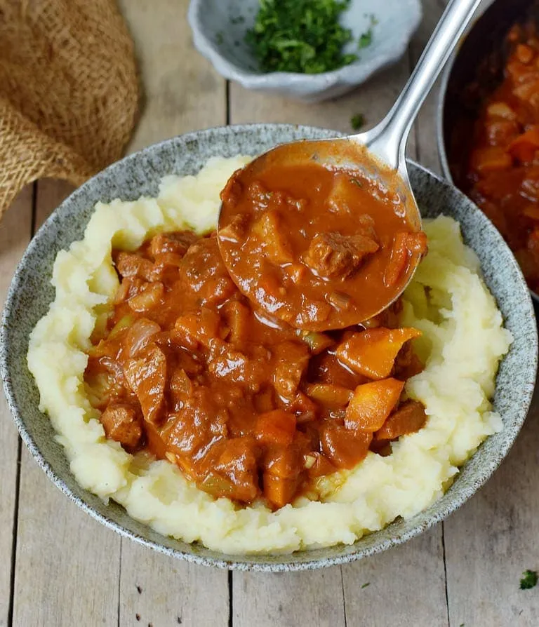 Veganes Gulasch mit Kartoffelbrei in einem Teller mit Schöpfkelle