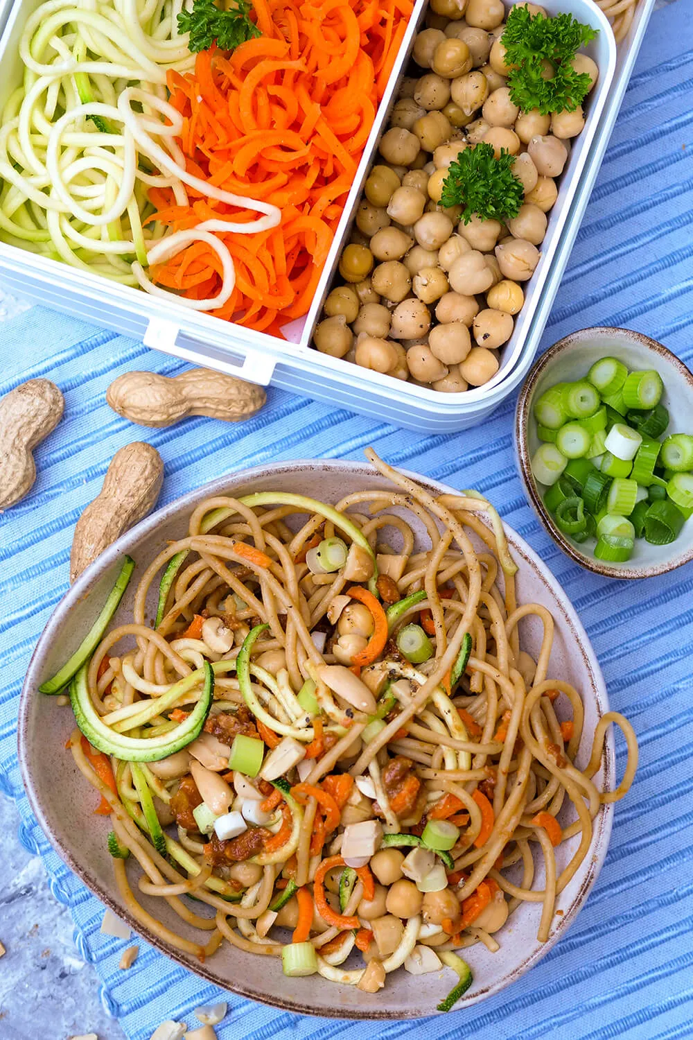 Vegetarische Erdnuss-Nudel-Bowl mit Vollkornspaghetti, Zucchininudeln und Kichererbsen, perfekt für das Mittagessen im Büro.