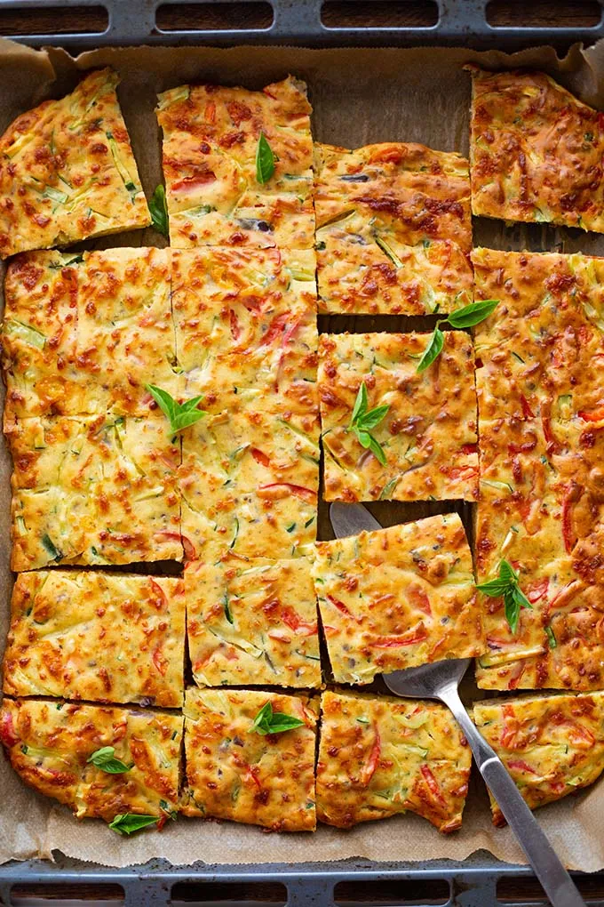 Vegetarische Quiche mit viel Gemüse auf einem Backblech. Geschnitten wie quadratische Kuchen Stücke und mit einem Tortenheber.
