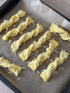 Verdrehte Käsestangen auf dem Backblech, bestrichen mit Eigelb und mit Käse bestreut, bereit für den Ofen.