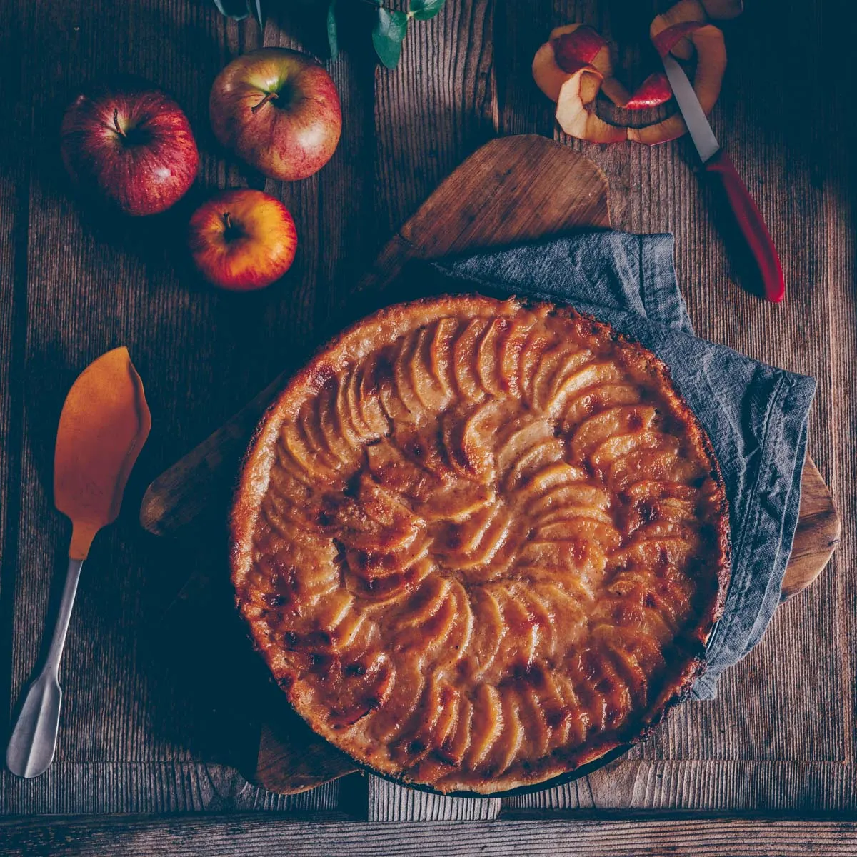 Verschiedene Apfelsorten, bereit zum Schälen und Schneiden, liegen nebeneinander auf einer Arbeitsfläche.
