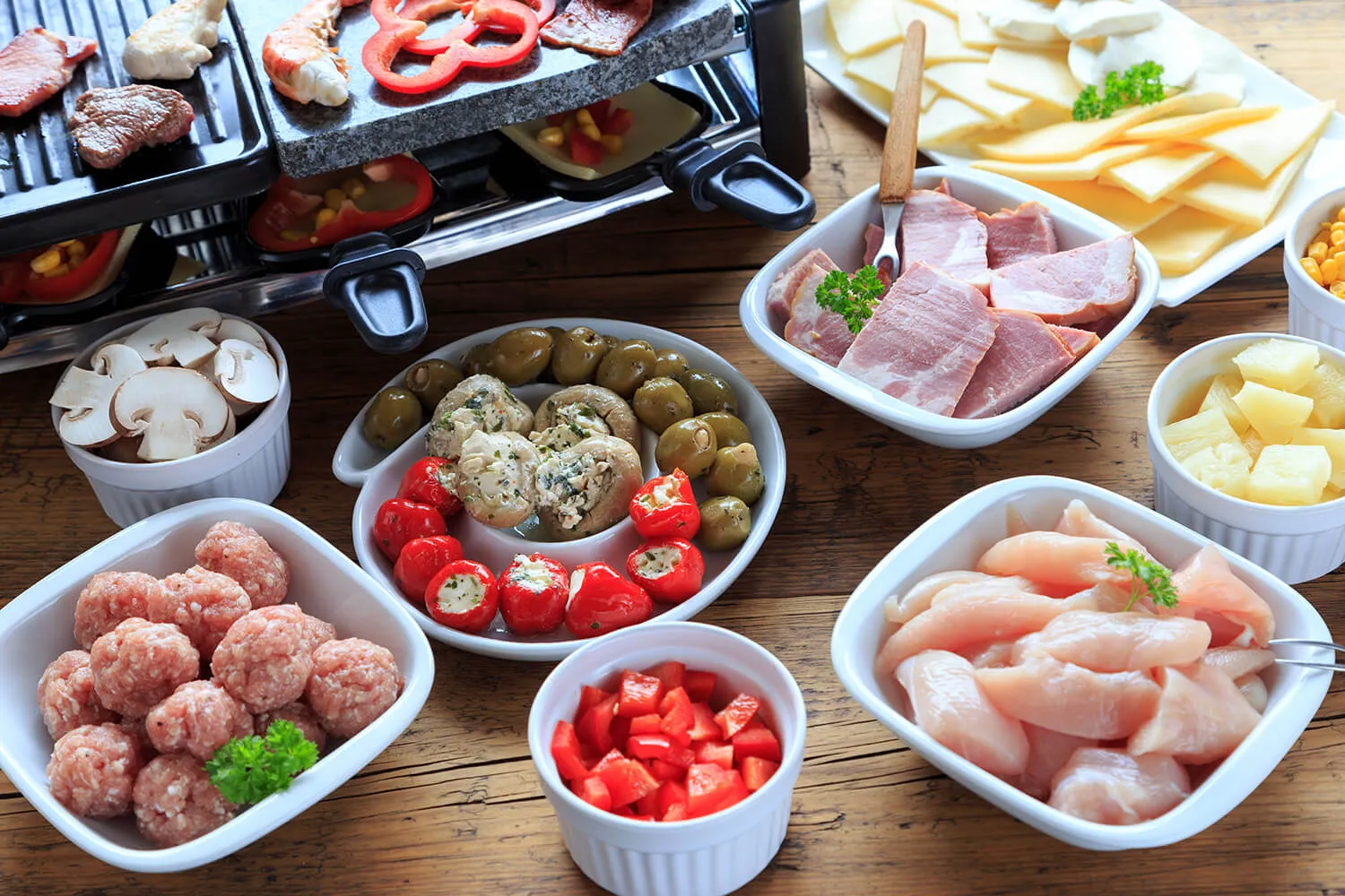 Verschiedene Raclette-Zutaten, darunter Fleisch, Käse und Gemüse, arrangiert auf einem Tisch