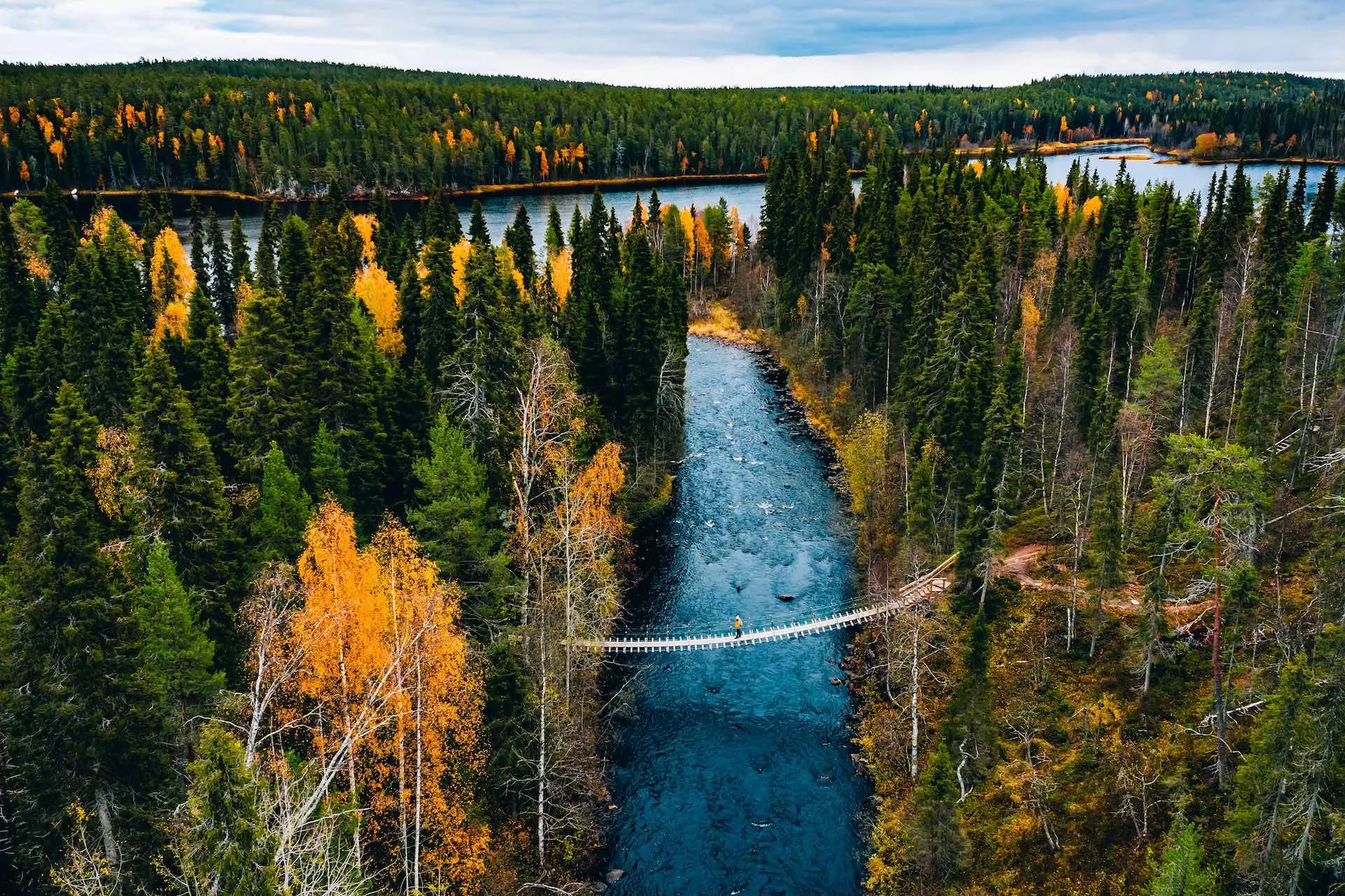 Verschneite Winterlandschaft in Lappland, Finnland, mit einem Fluss und Nadelbäumen unter blauem Himmel