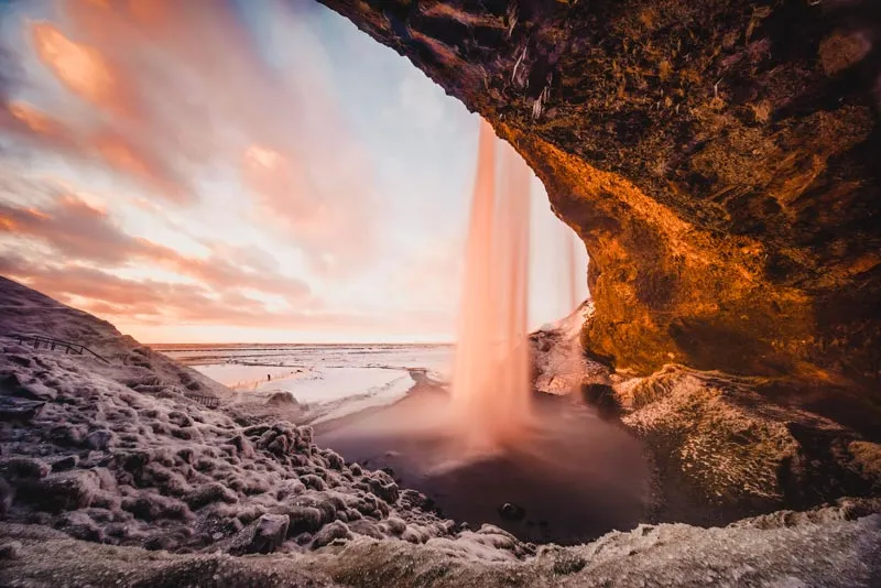 Verschneite Winterlandschaft Islands mit einem majestätischen Wasserfall bei Sonnenuntergang im März
