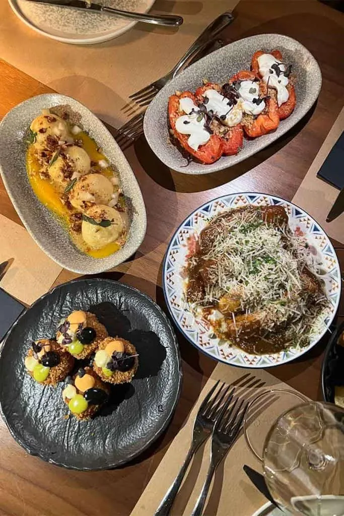 Vielfältige Tapas-Gerichte von SOL Tapas in Zagreb, darunter Knödel in gelbem Püree, Tomaten mit Sahne, ein herzhaftes Fleischgericht mit geriebenem Käse und knusprige Garnelenkroketten, appetitlich auf einem Tisch arrangiert.