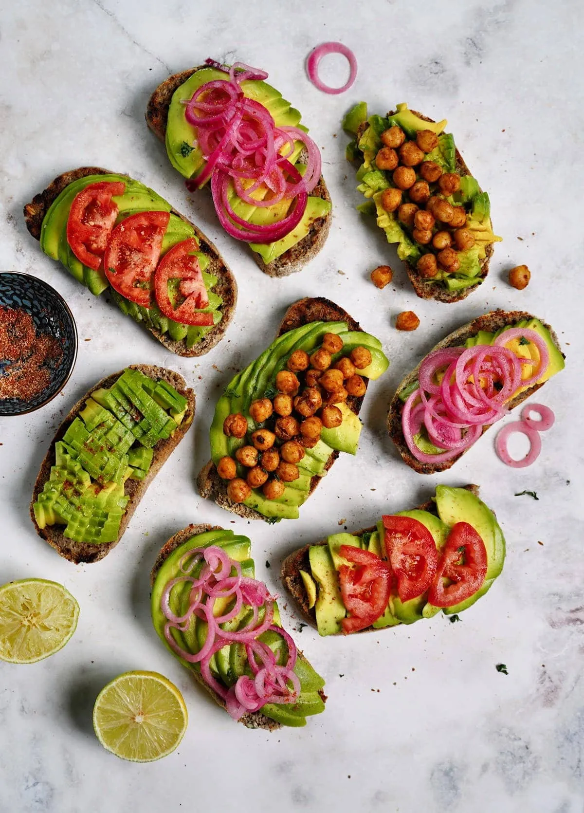 Vielseitig belegter Avocado-Toast auf weißem Marmor mit bunten Toppings, eine leichte und nährstoffreiche Idee für ein veganes Mittagessen.