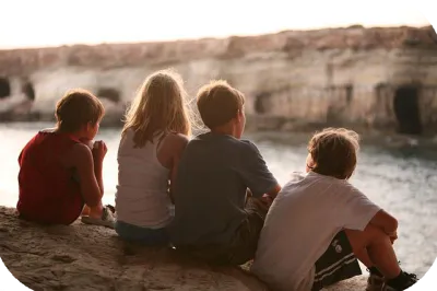 Vier Kinder sitzen auf einer Felsklippe und blicken auf das weite Meer