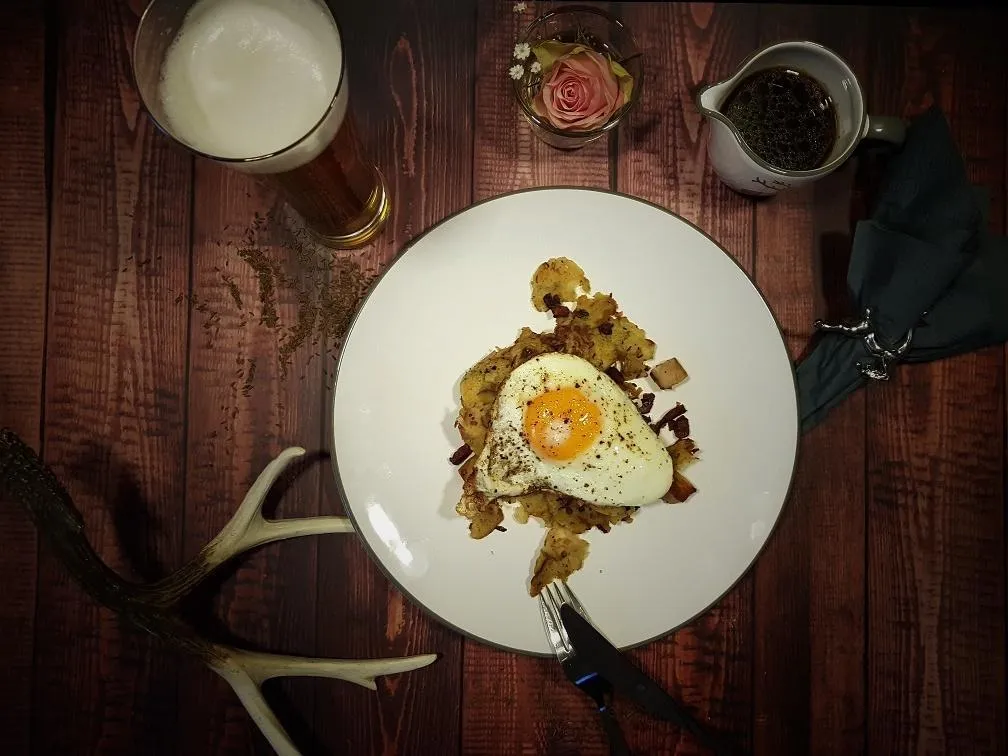 Von oben fotografiertes, frisch zubereitetes Tiroler Gröstl mit goldbraunen Kartoffeln, Fleisch und Spiegelei