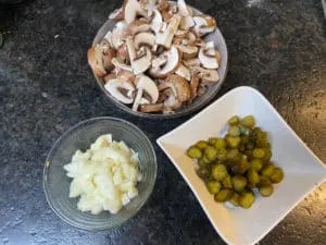 Vorbereitete Zutaten für Stroganoff: gewürfelte Zwiebeln, geschnittene Champignons und Essiggurken