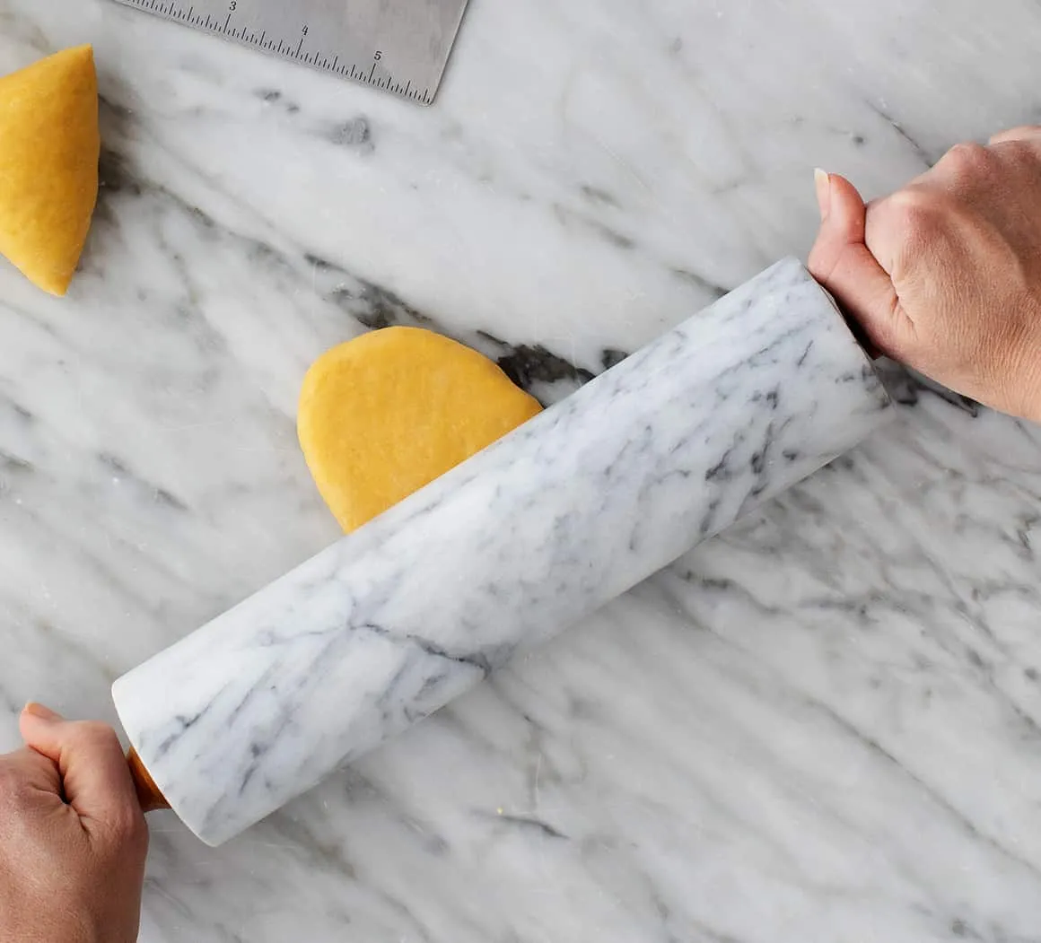 Vorsichtiges Ausrollen eines Teigstücks für Linguine mit einem Nudelholz, bevor es durch die Nudelmaschine geführt wird.