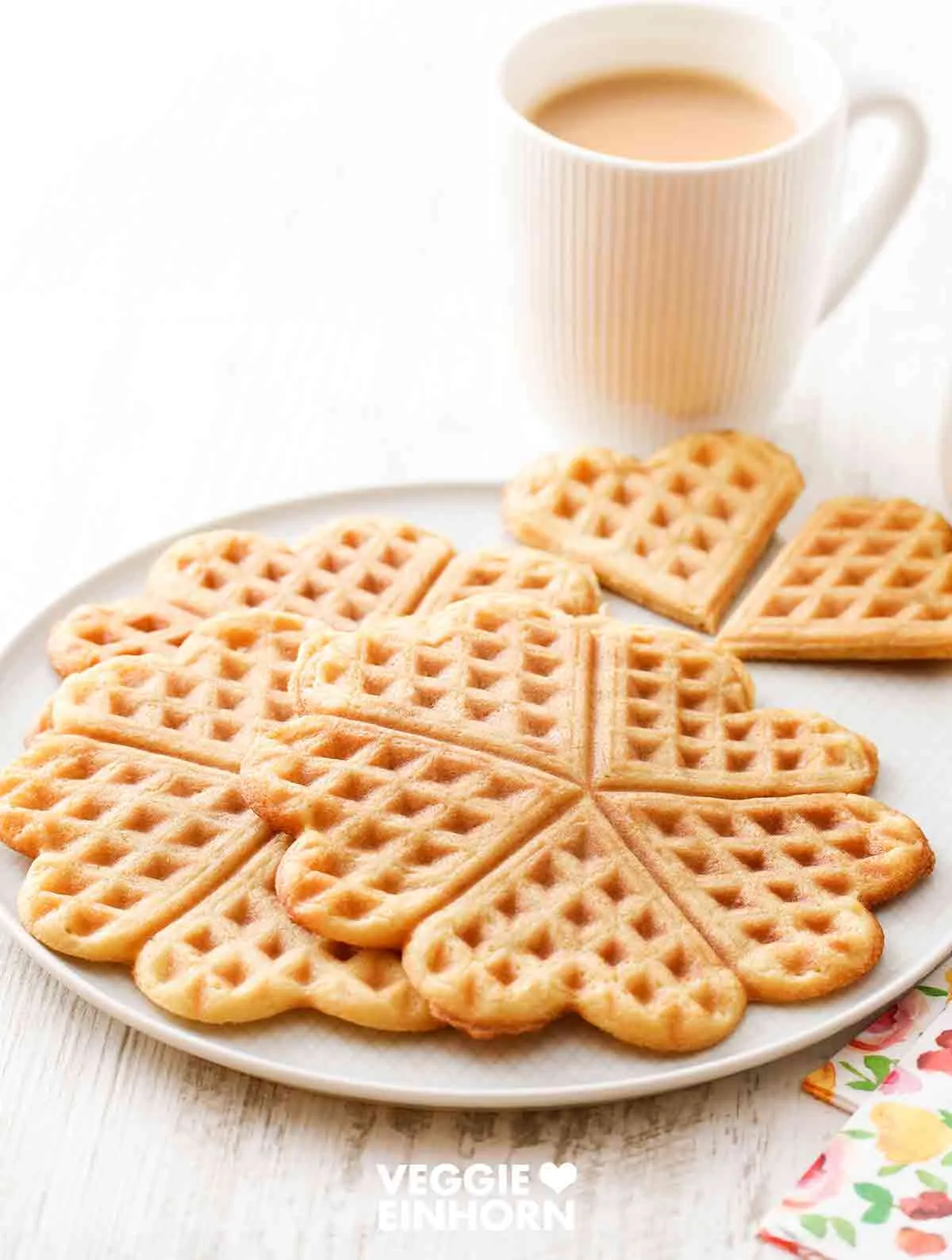 Waffeln ohne Ei auf einem Teller, im Hintergrund eine Tasse mit Milchkaffee