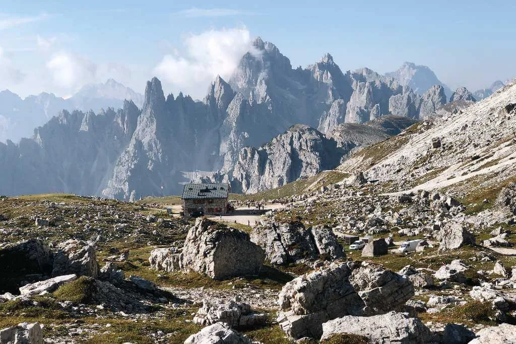 Wanderer genießen den Blick auf die Drei Zinnen vom Rifugio Lavaredo aus. Die majestätischen Gipfel erheben sich über die grüne Landschaft.