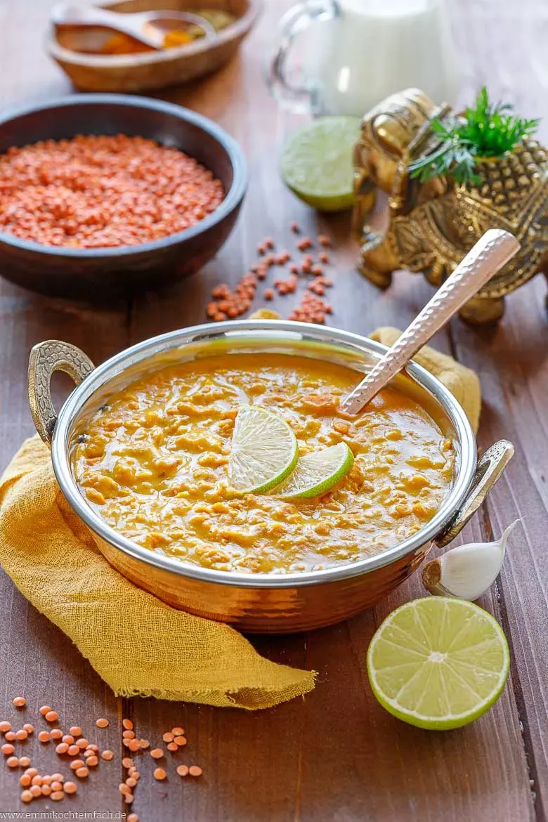 Wärmende rote Linsensuppe mit Kokosmilch in einer weißen Schale, garniert mit frischer Petersilie und Limettenspalten, bereit zum Genuss.