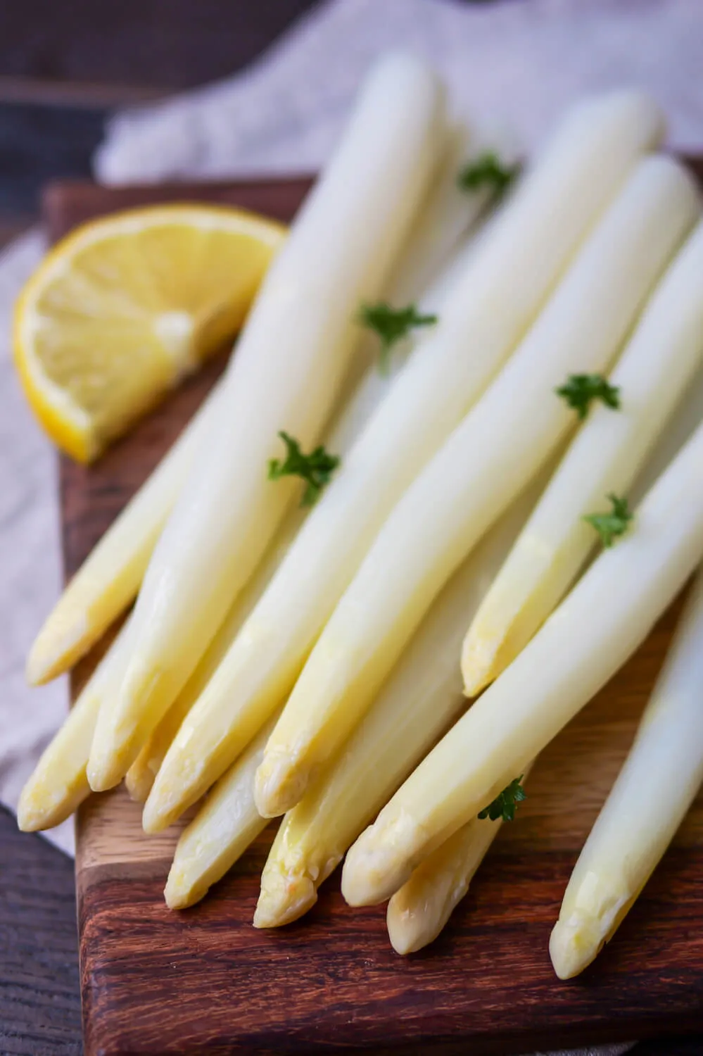 Weißer Spargel mit Petersilie und Zitrone auf einem Holzbrett.