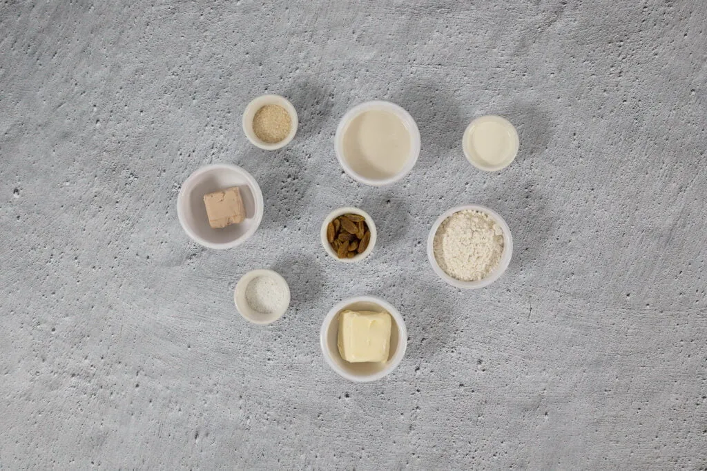 Wichtige Zutaten für Hefeteig-Glücksschweinchen: Mehl, Hefe und getrocknete Weintrauben (Sultaninen) auf einem Holztisch.