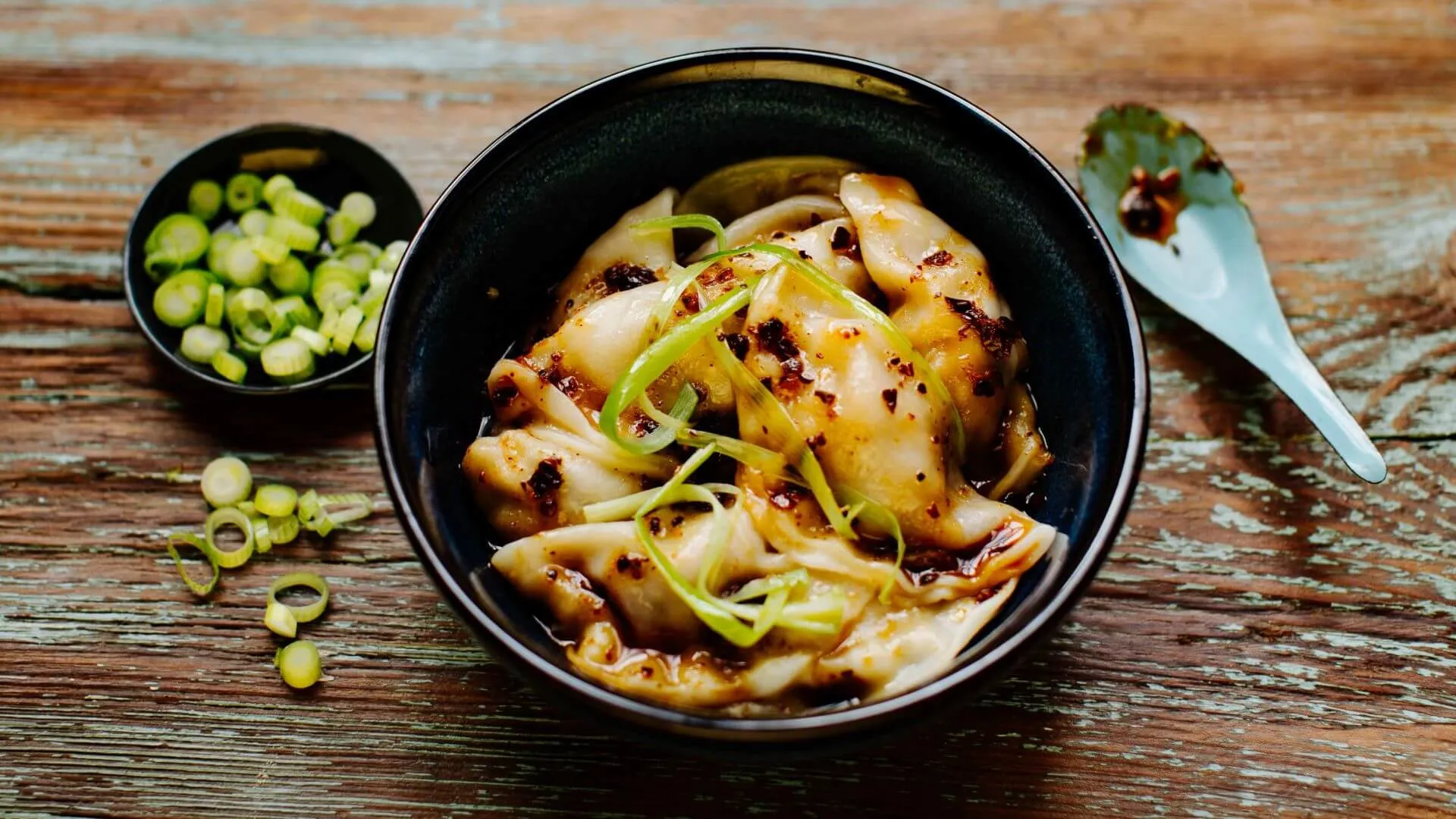Würzige Wantan-Teigtaschen in glänzendem Chili-Öl nach Szechuan-Art, garniert mit frischen Kräutern, ein authentischer chinesischer Snack
