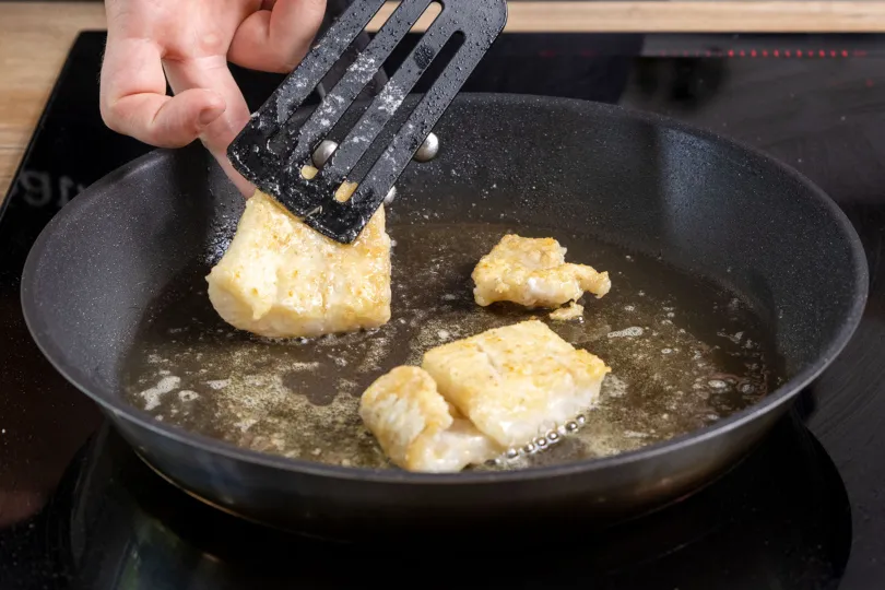 Zartes Kabeljaufilet brät goldbraun in der Pfanne, bereit für einen köstlichen deutschen Fischgenuss.