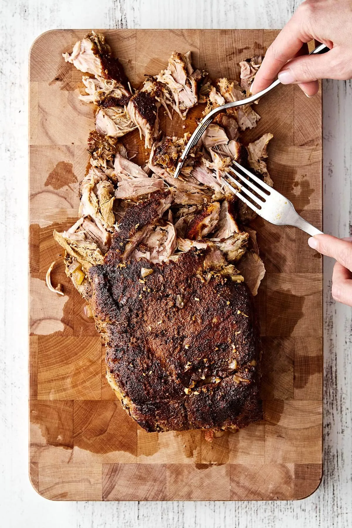 Zartes Pulled Pork wird nach dem Garen auf einem Schneidebrett zerzupft.