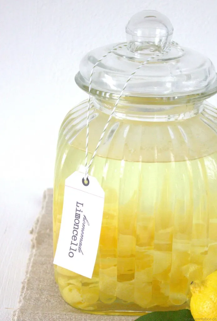 Zitronen als Hauptzutat für die Limoncello-Herstellung, mit einer fertigen Flasche im Hintergrund.